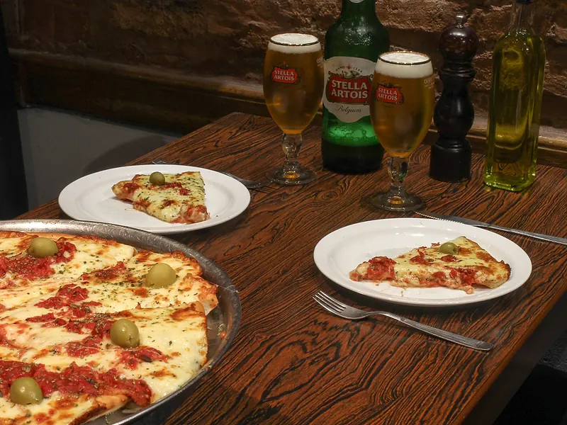 Pizza de muçarela com azeitonas e cerveja em uma mesa da Don Boedo